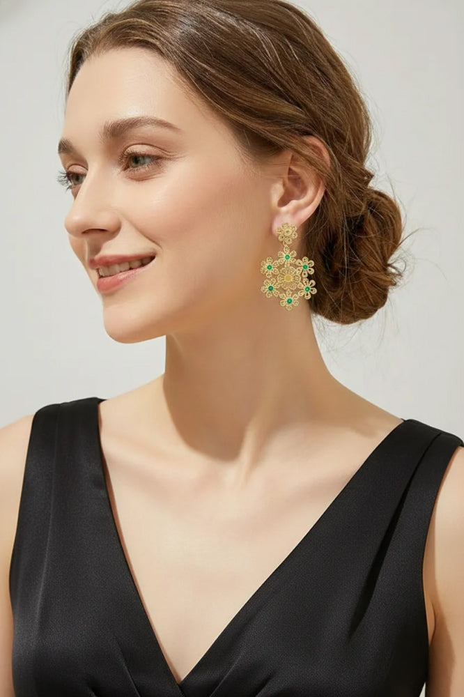 Woman wearing gold earrings with green gemstones against a plain background