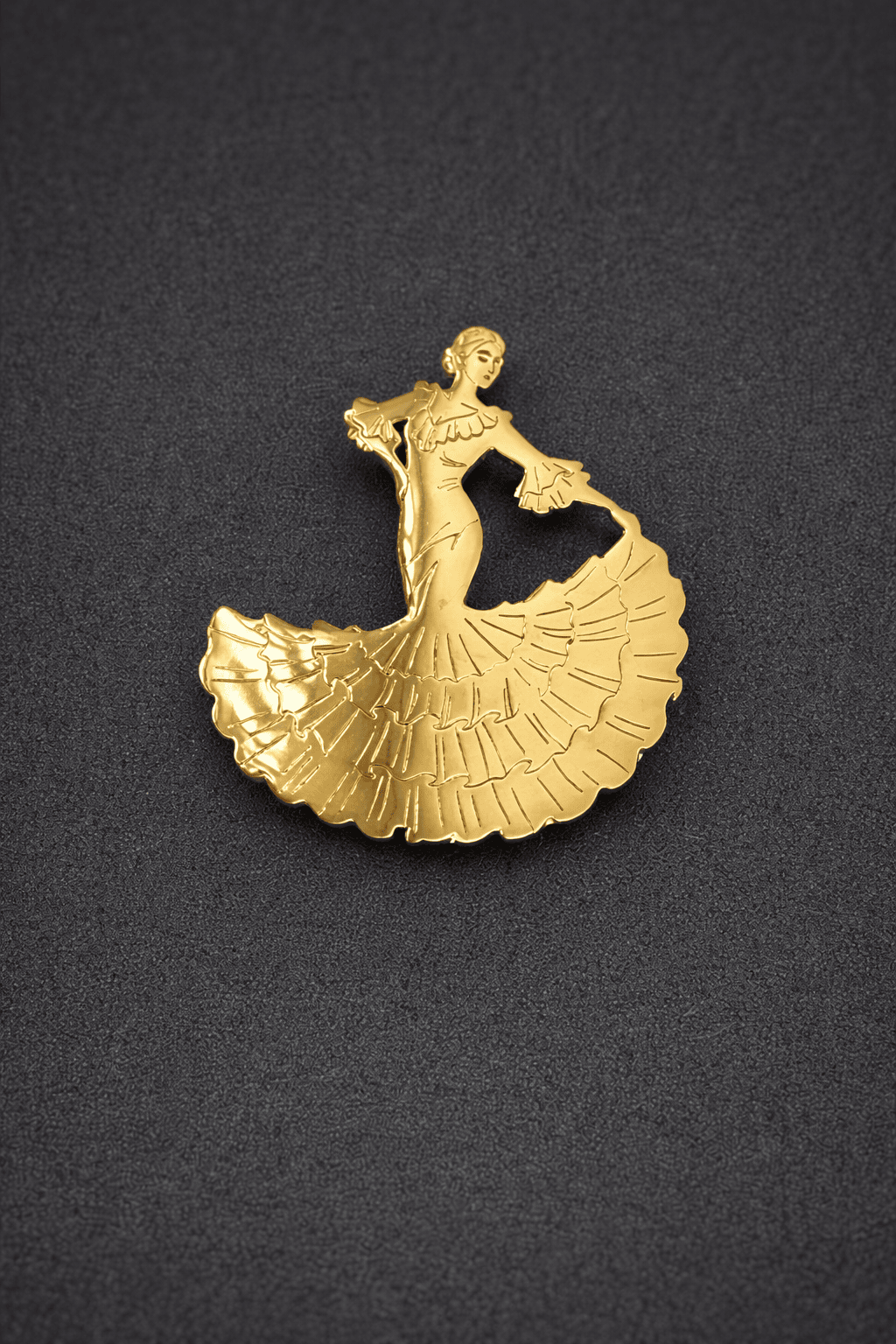 Gold brooch of a dancer on a textured black background