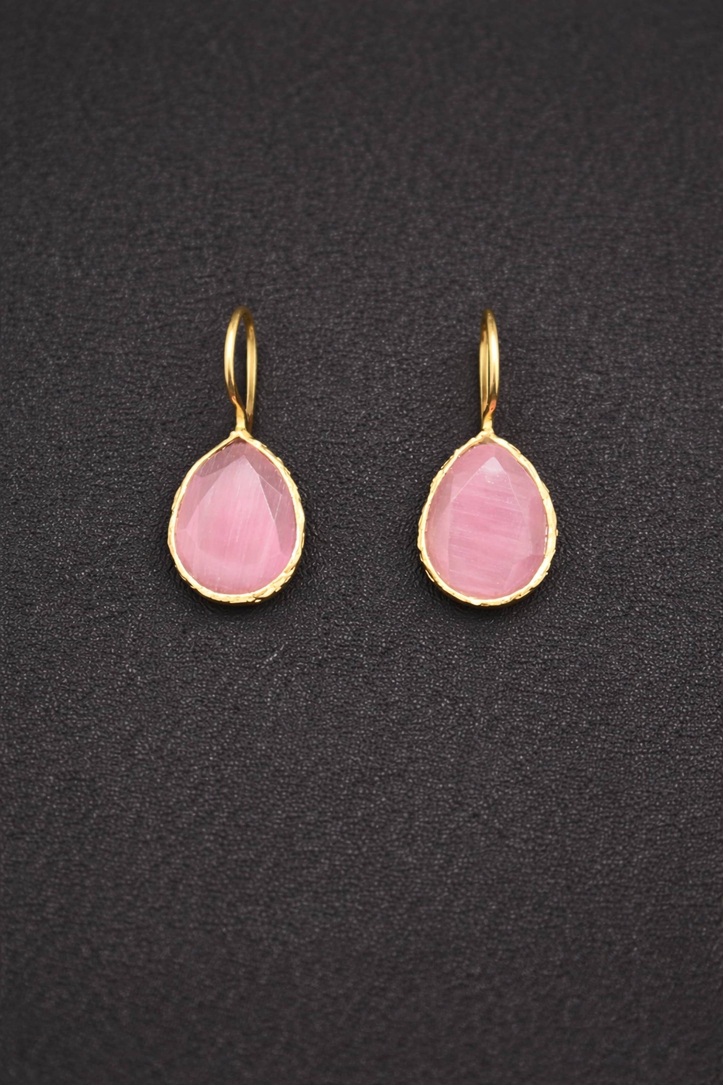 Pair of pink teardrop earrings with gold hooks on a dark textured background