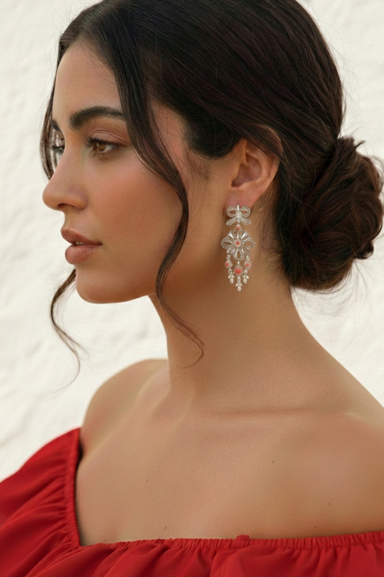 Woman wearing a pair of silver earrings with a red top against a neutral background