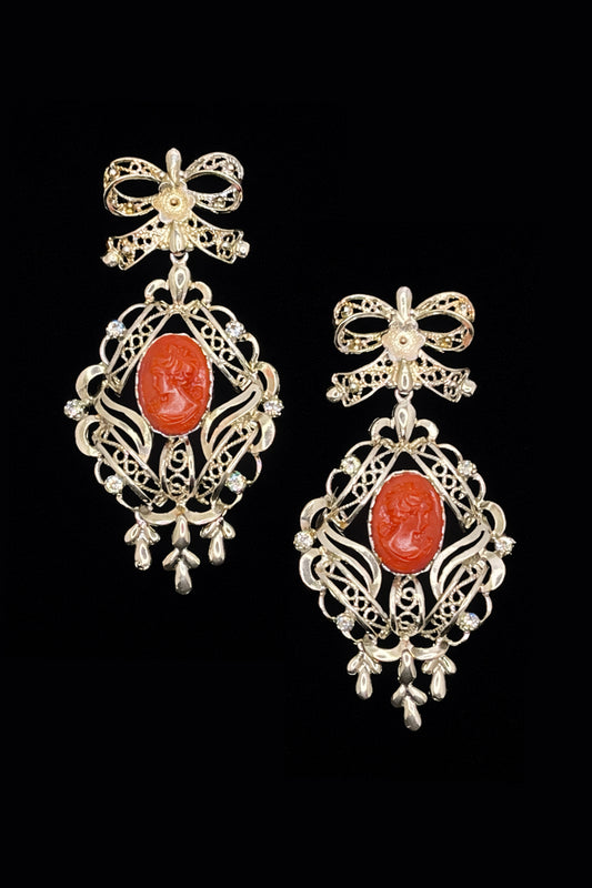Pair of ornate earrings with red stones on a black background