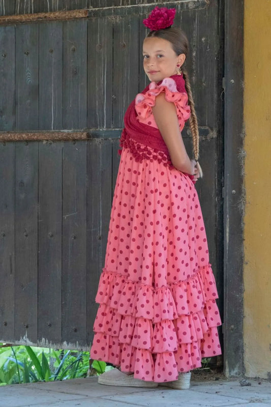 Young girl in a pink dress with ruffles standing against a rustic wooden door.