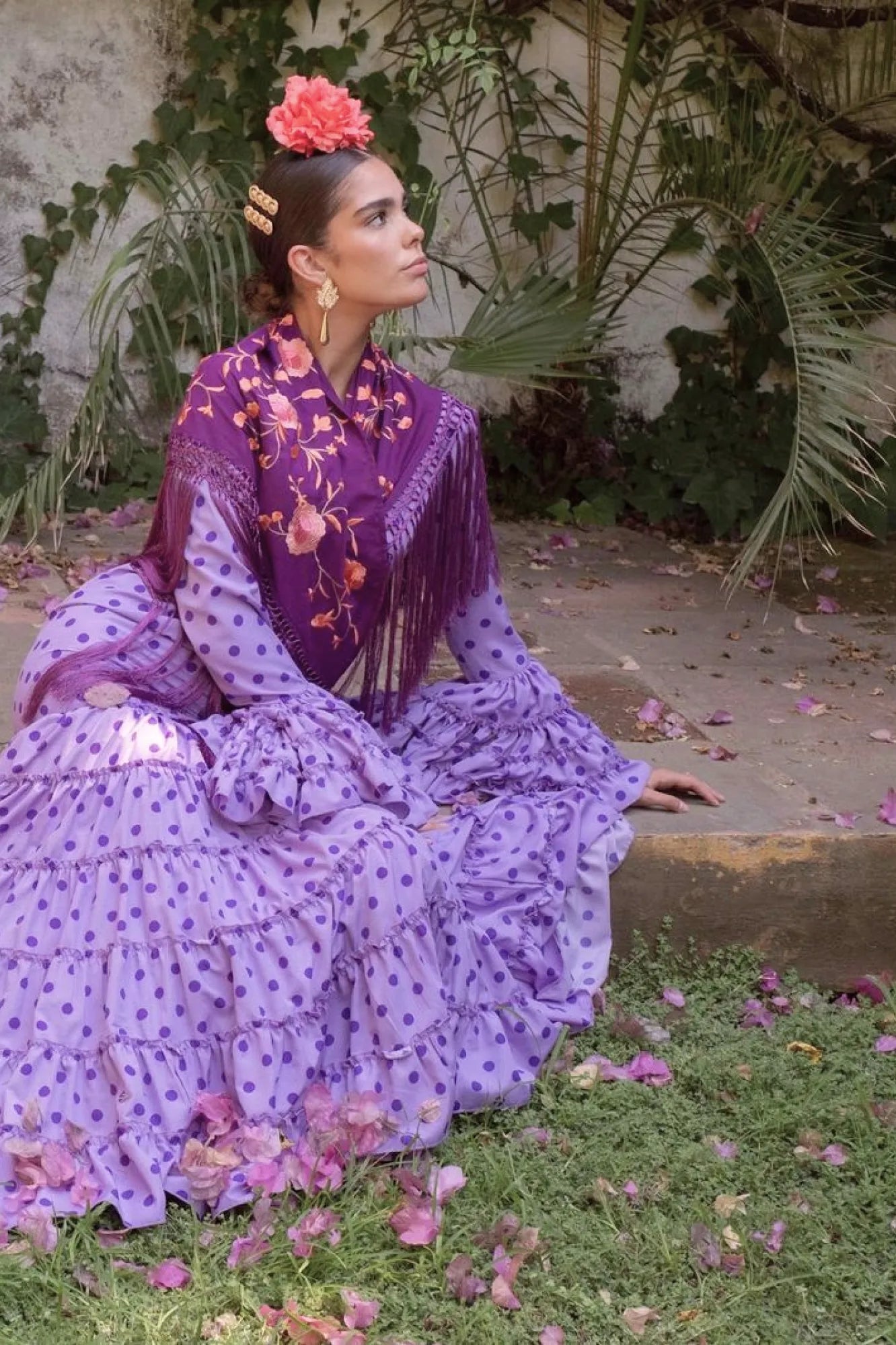 Woman in a purple traditional outfit sitting on grass with flowers.