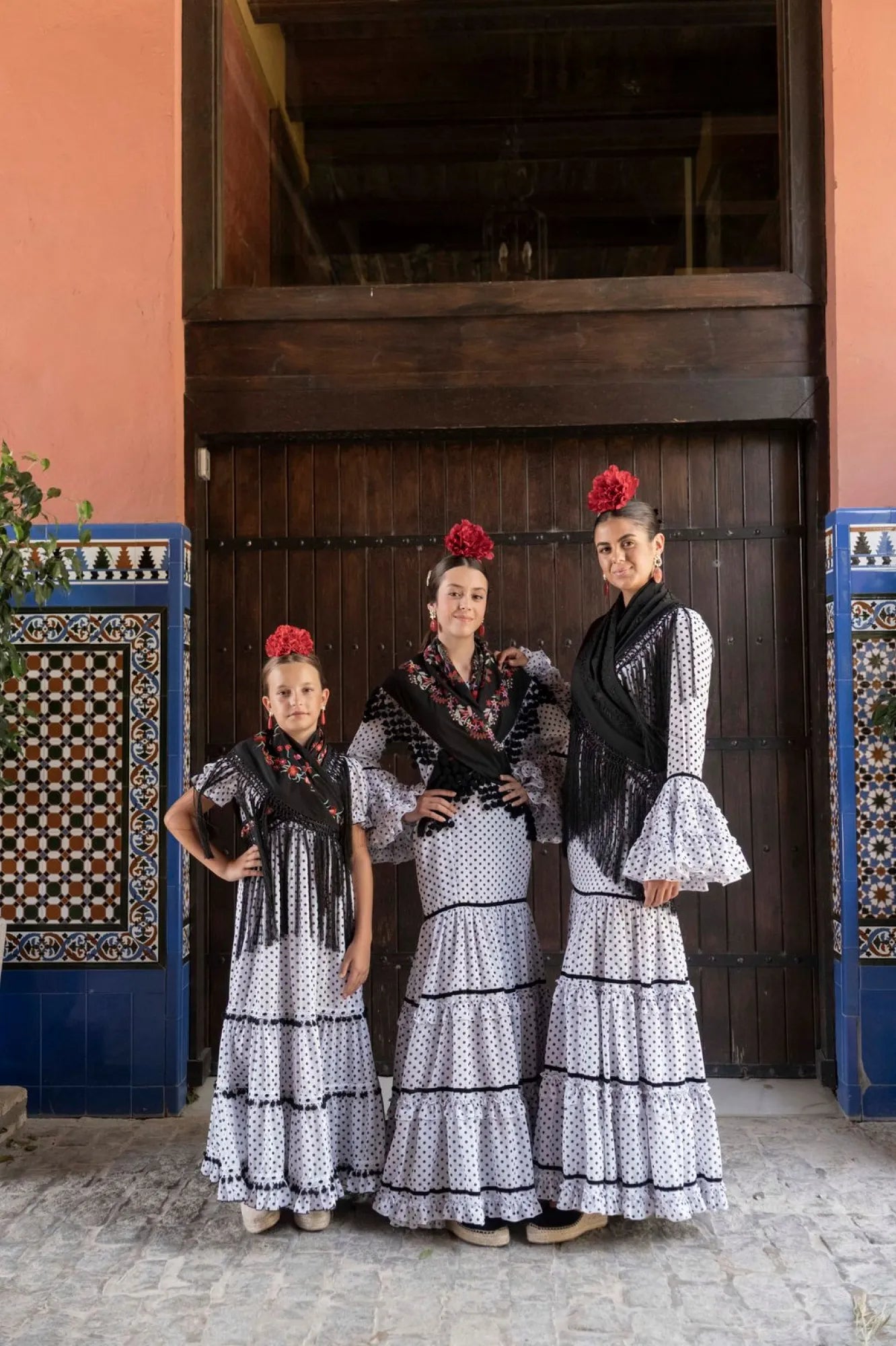 Three women in traditional dresses standing in front of a wooden door with decorative blue panels.