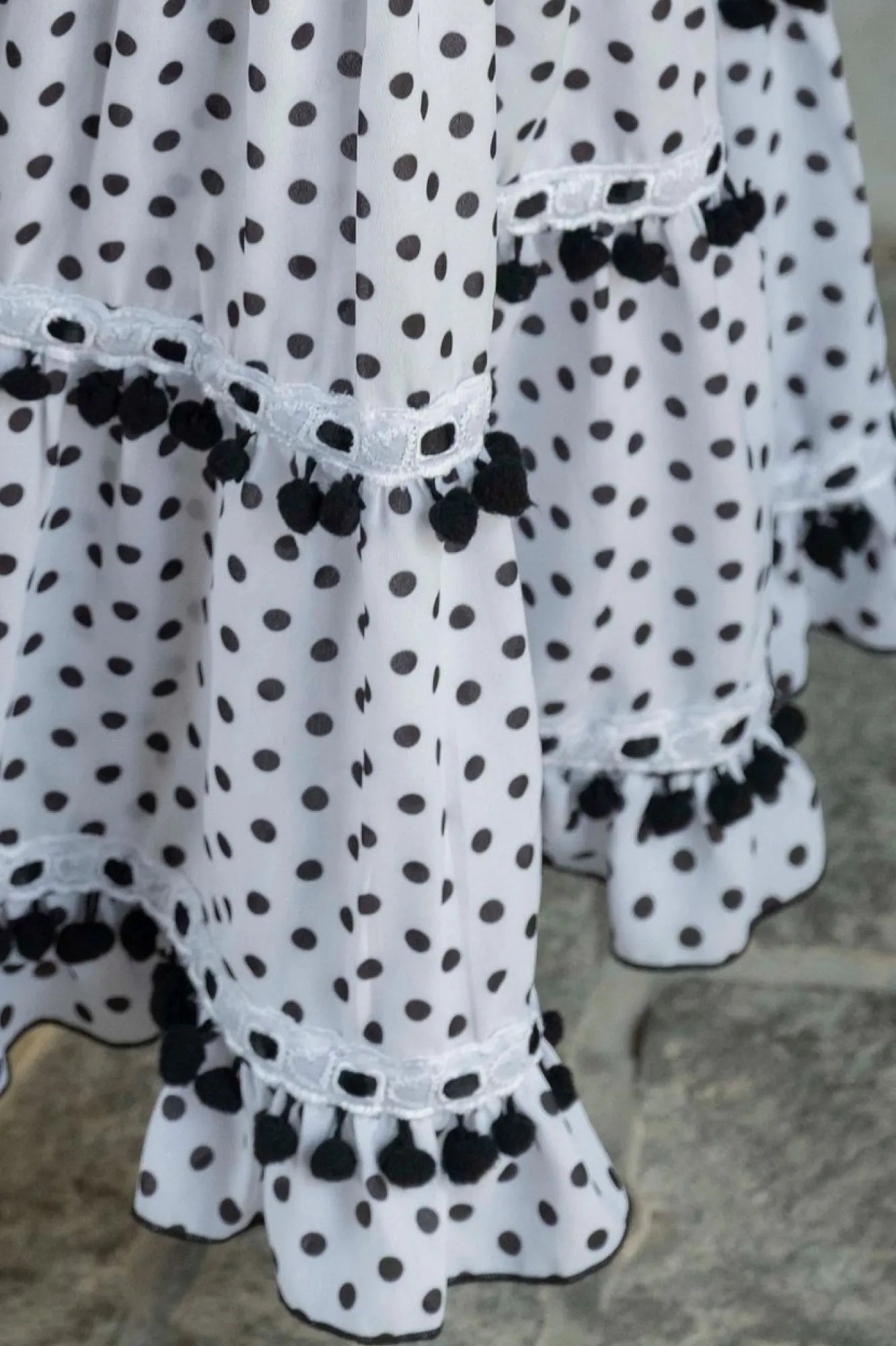 White dress with black polka dots and pom-pom details on a textured surface