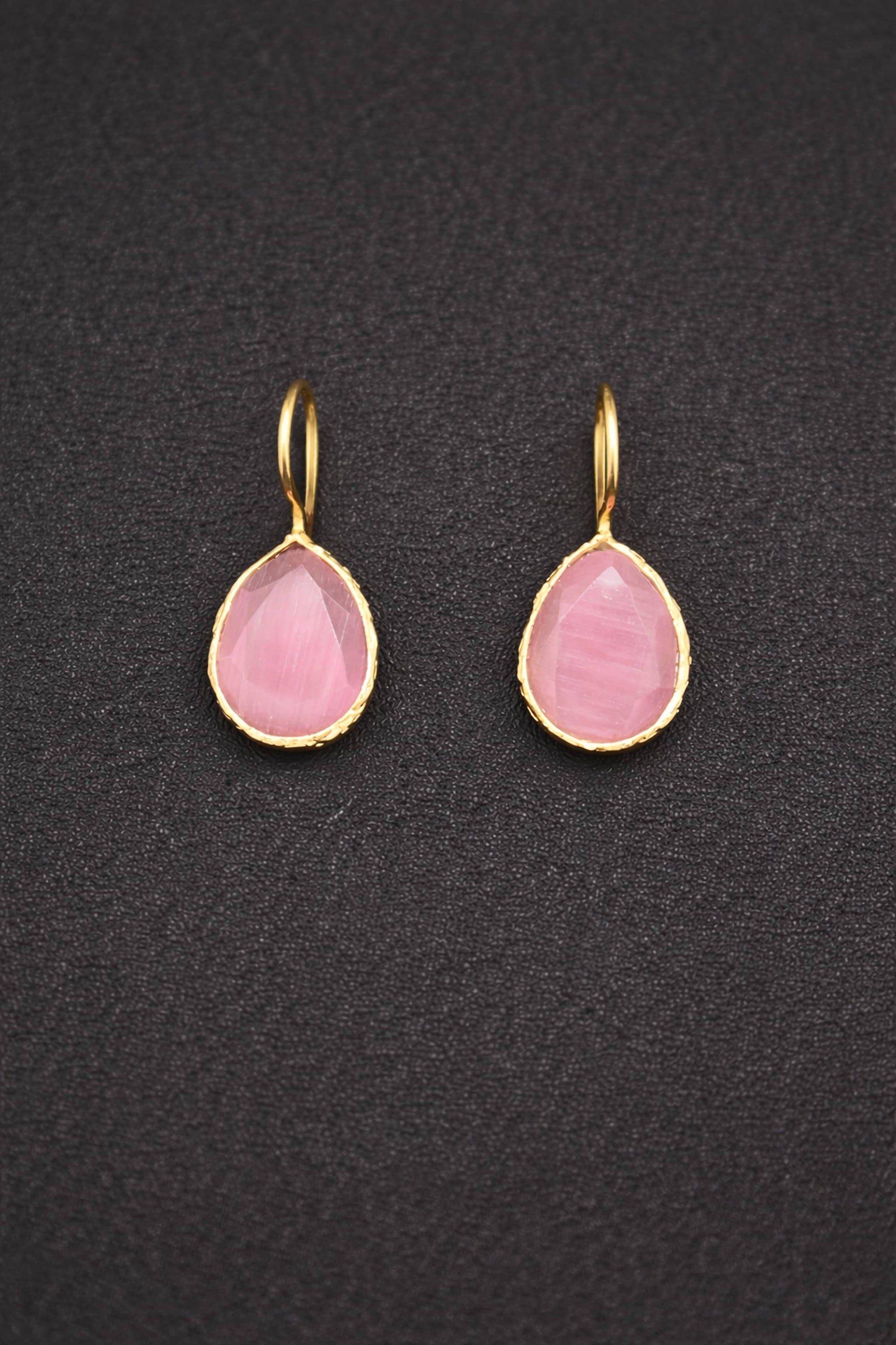 Pair of pink teardrop earrings with gold hooks on a dark textured background