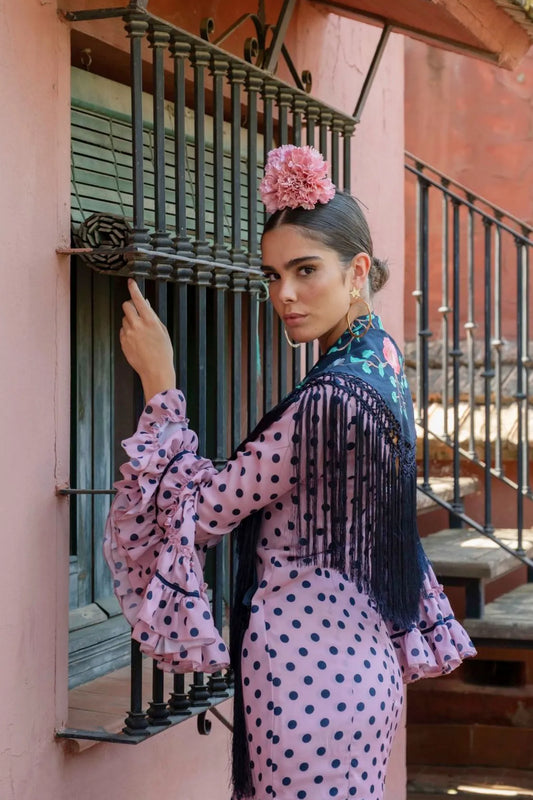 Woman in a polka dot dress with floral headpiece standing in front of a pink building.