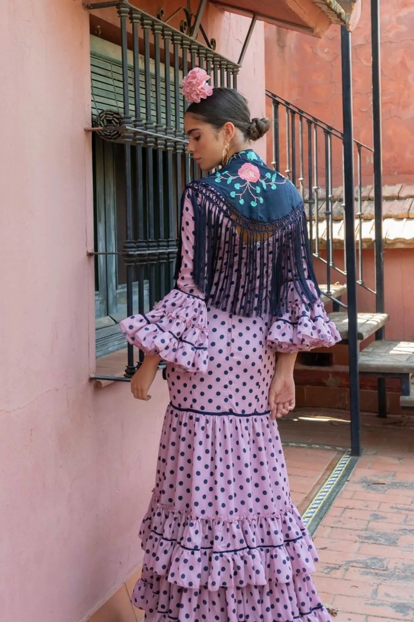 Woman in a traditional outfit with floral headpiece standing in front of a pink wall.